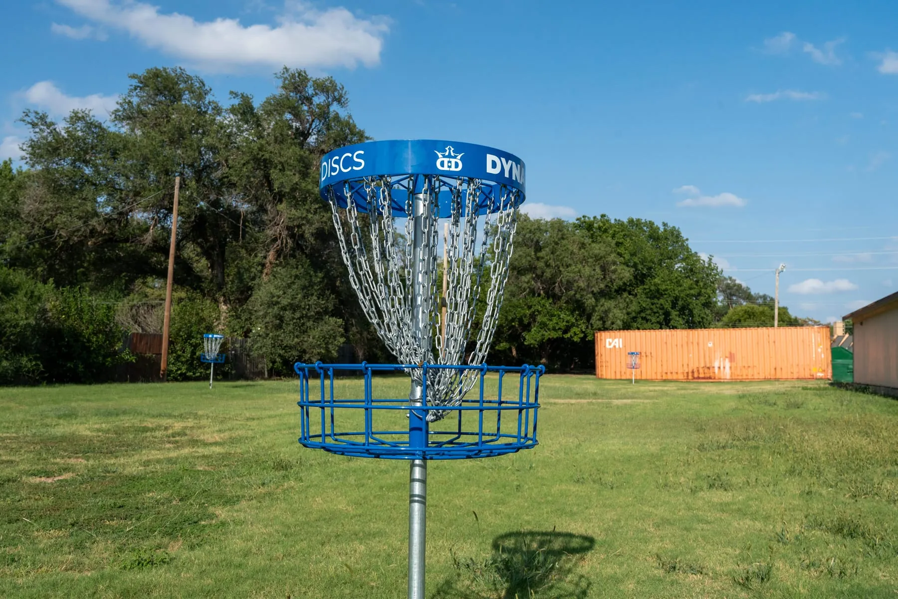 A disc golf basket on the mown field at Stoneybrook, with a second basket beyond it.