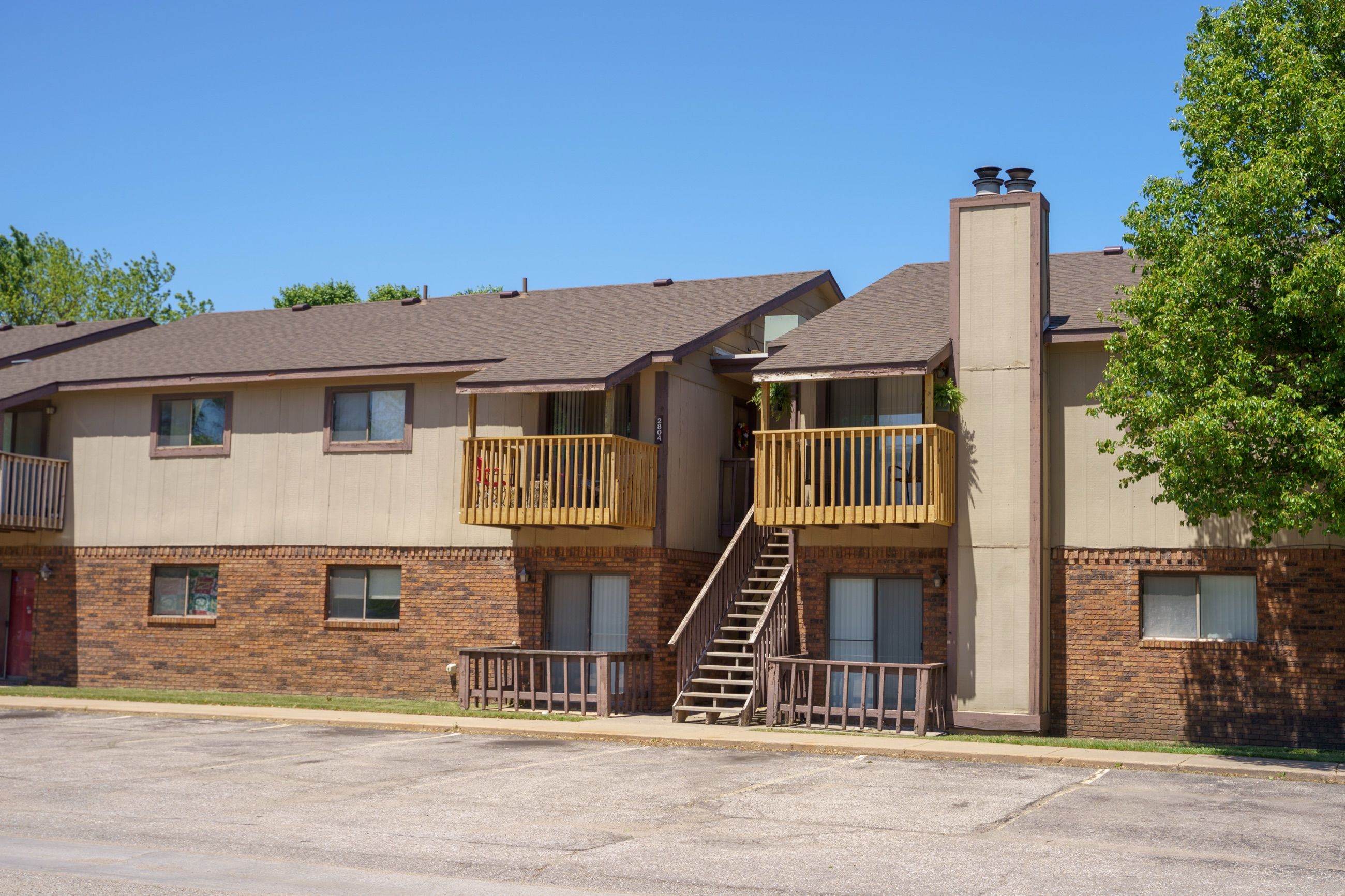 Two-story brick and cedar-sided apartment building at Stoneybrook with private balconies, under a clear Kansas sky.