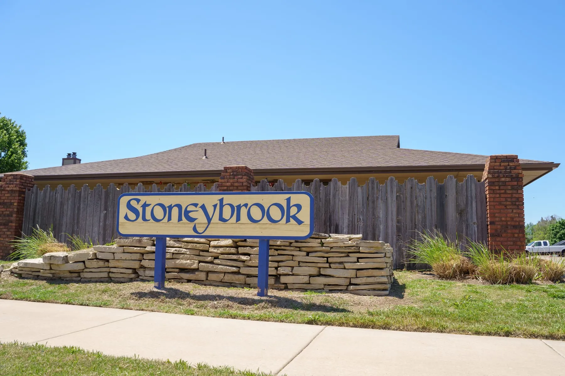 The Stoneybrook monument sign at the entrance, a cream panel with royal-blue lettering on a stacked Kansas limestone base.
