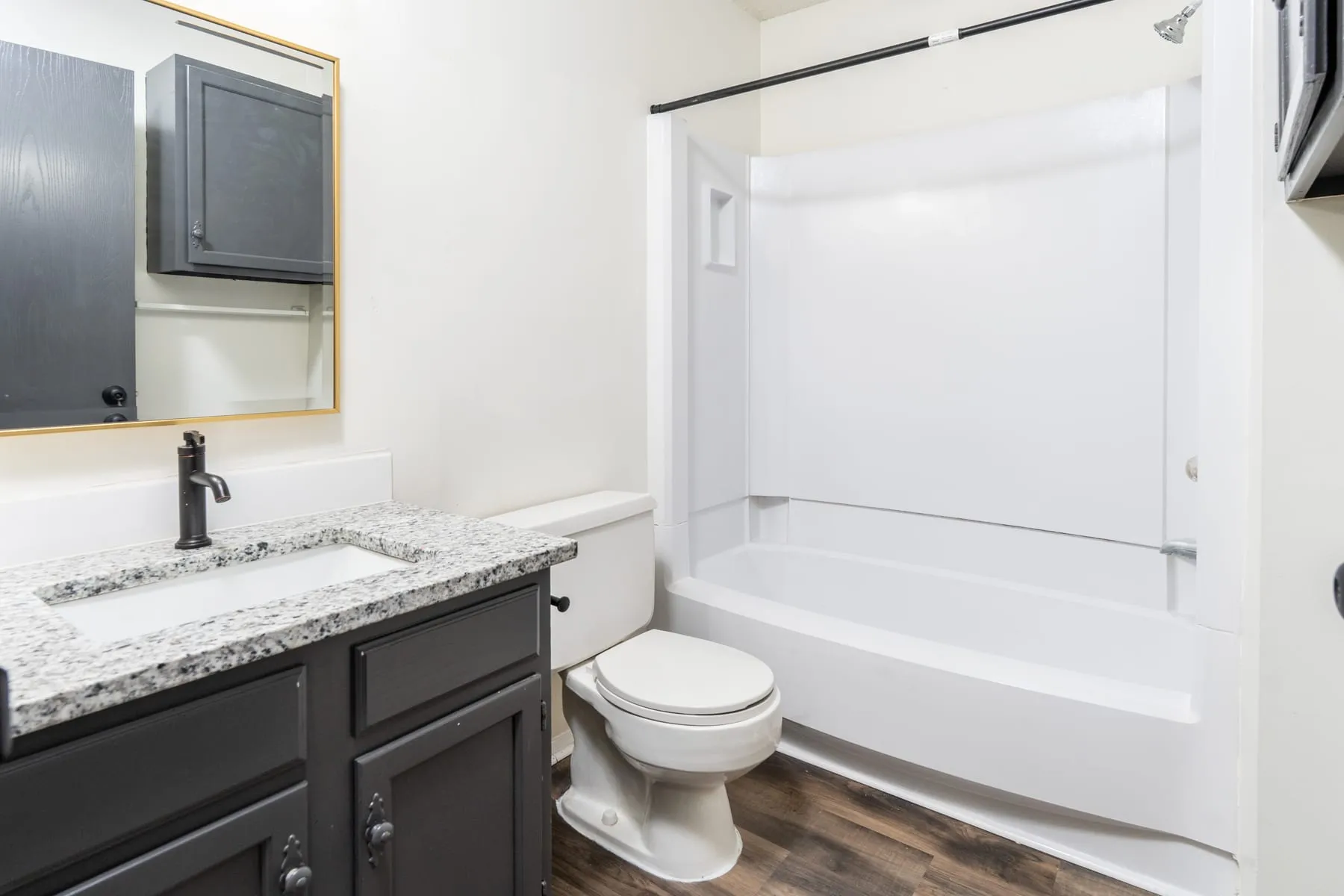 Renovated one bedroom bathroom with granite vanity, framed mirror and tub surround.