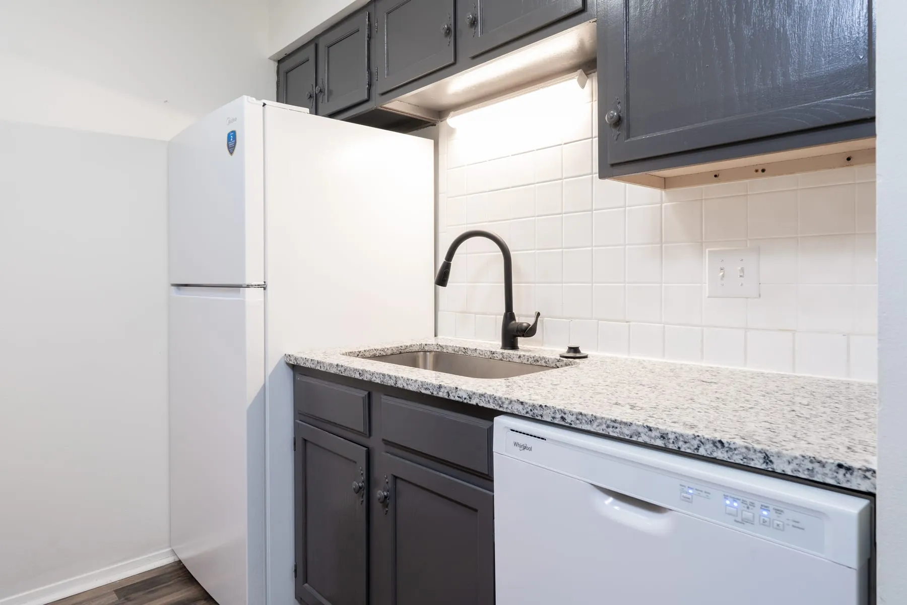 Stainless sink and matte black faucet against white subway tile in a one bedroom kitchen.