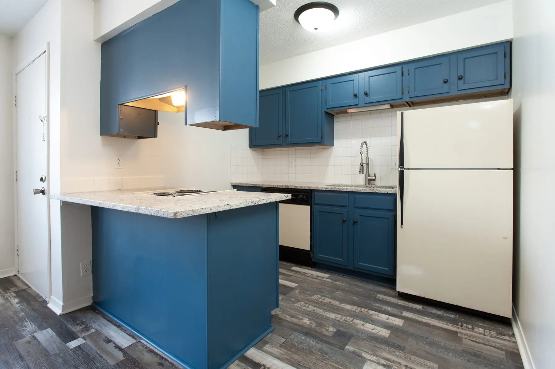 Petrol-blue kitchen cabinetry and granite peninsula in a renovated studio.
