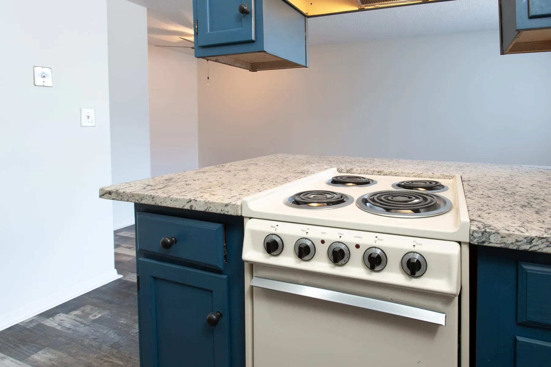 Studio kitchen range and granite counter beneath petrol-blue upper cabinets.