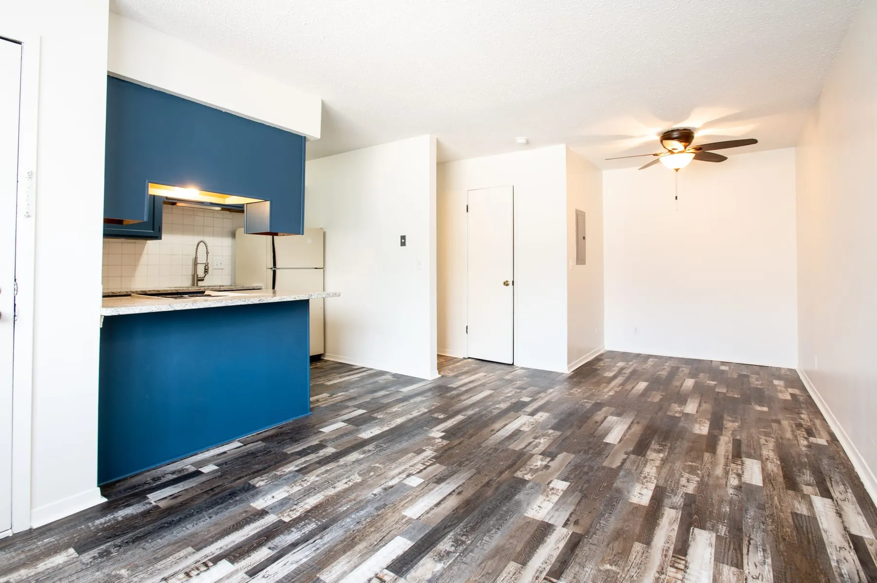 Studio living area with ceiling fan and driftwood-tone plank flooring.