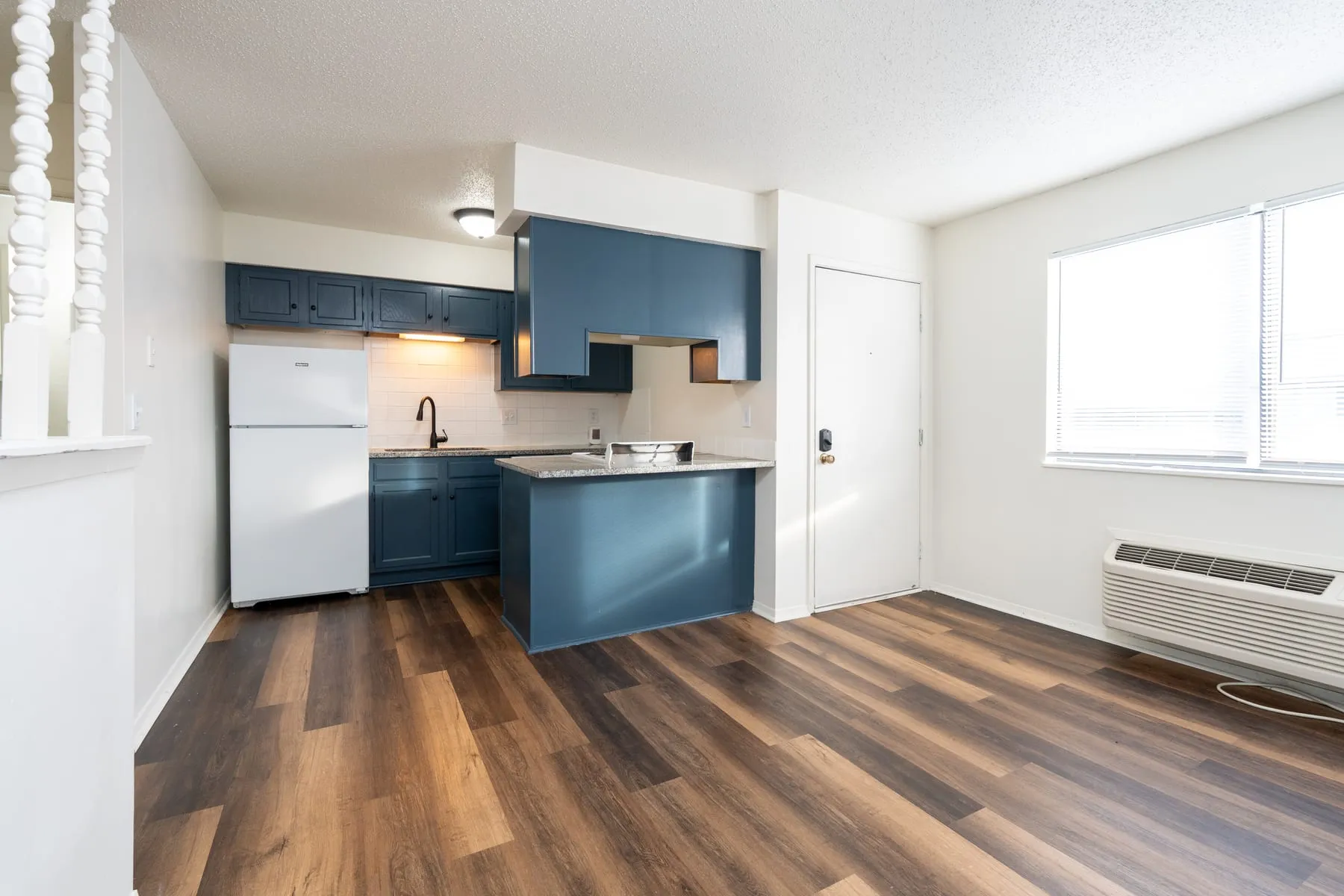 Studio kitchen with petrol-blue cabinetry, granite counters and a full-size refrigerator.