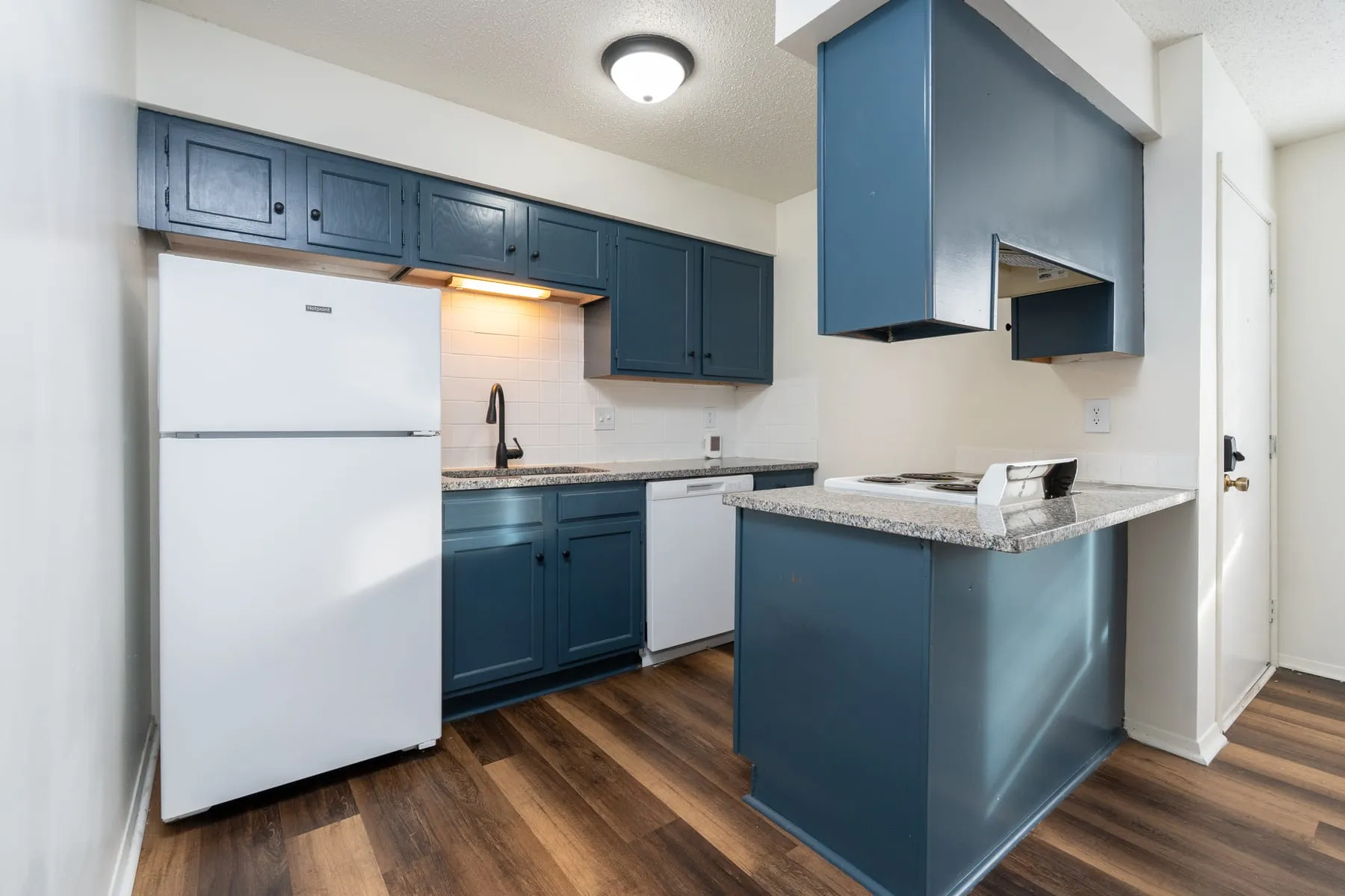 Studio kitchen showing the peninsula, dishwasher and upper cabinetry in petrol blue.