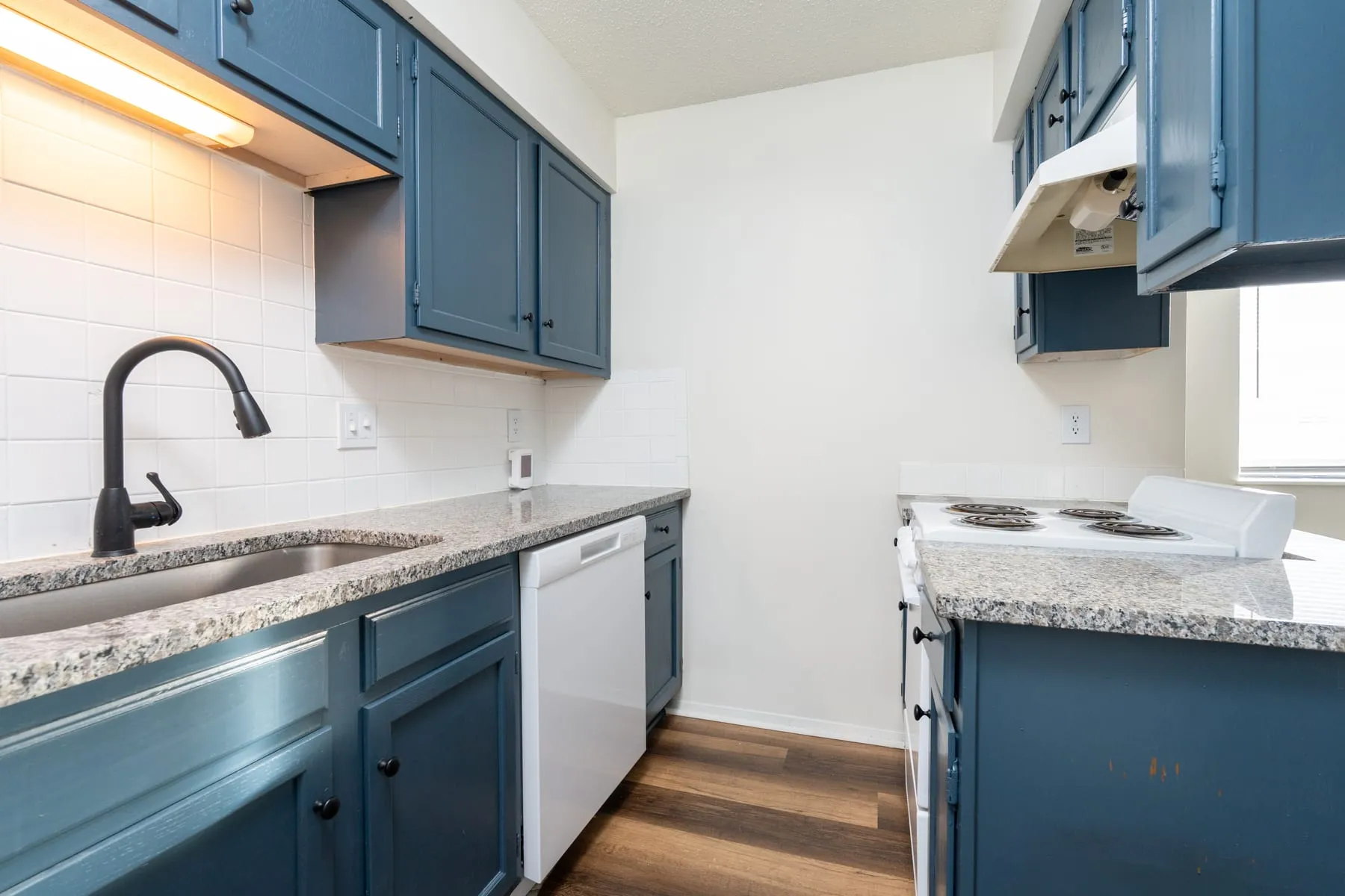 Stainless sink with a matte black faucet set into granite counters in a studio kitchen.