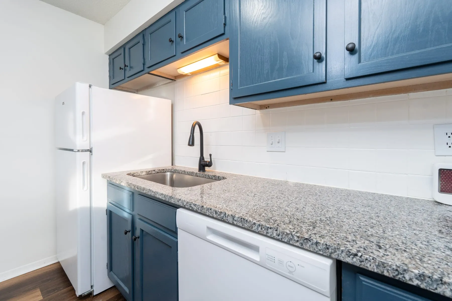Studio kitchen counter run with refrigerator, granite surface and subway tile.