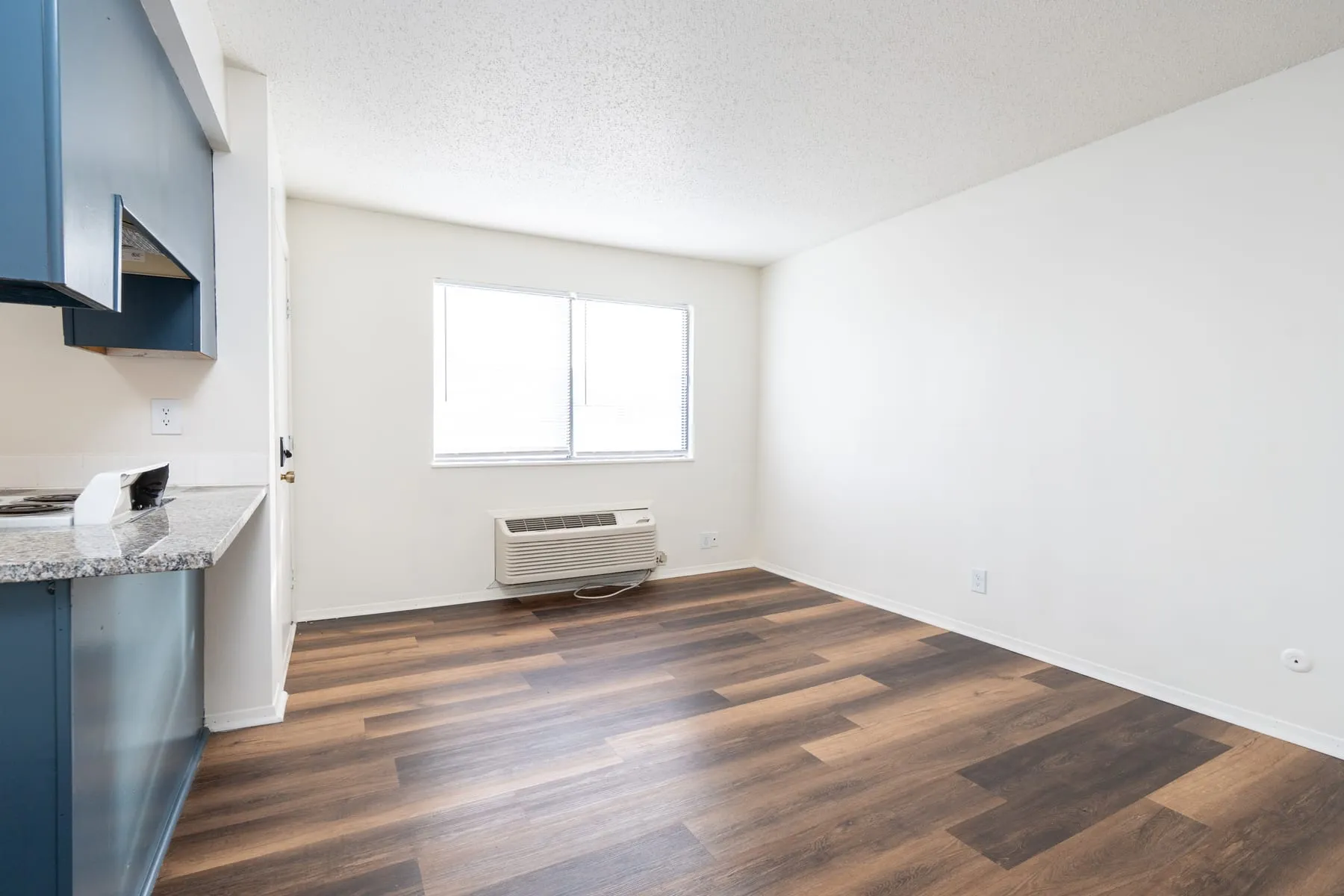 Studio living area with a large window and through-wall heating and cooling unit.